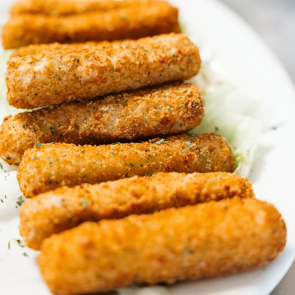 Close-up of golden-brown mozzarella sticks, lightly seasoned, served on a bed of shredded lettuce.