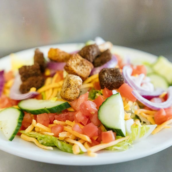 A vibrant Lena's Kitchen salad with lettuce, tomatoes, cucumbers, red onion, shredded cheese, and croutons.