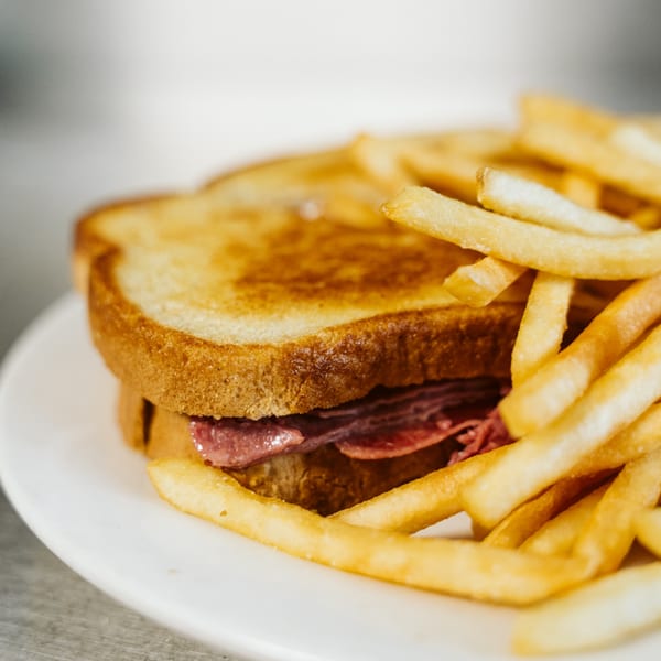 Close-up of a toasted sandwich with meat and a side of golden french fries on a white plate.