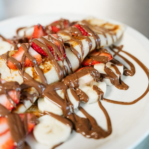 Crepes topped with sliced strawberries, bananas, and a generous drizzle of chocolate sauce.
