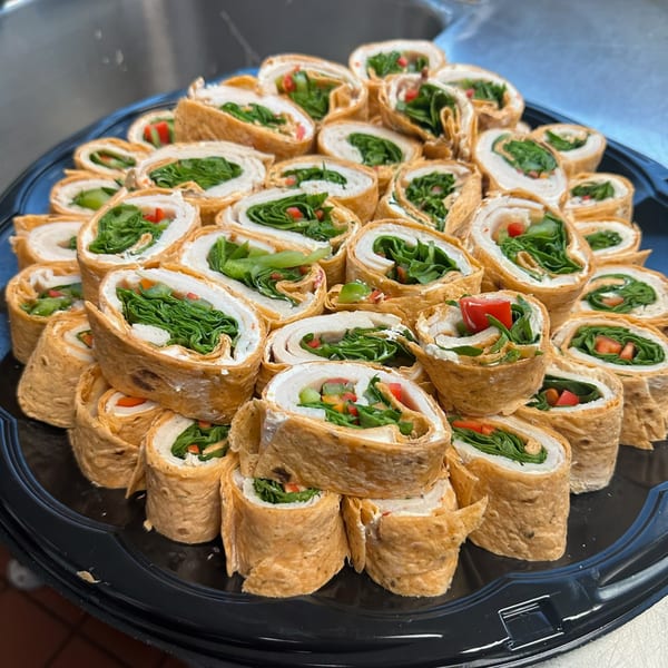 A catering tray of Lena's Kitchen American pinwheel wraps, filled with turkey, cream cheese, lettuce, and diced red peppers.