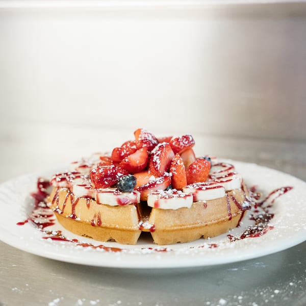 Lena's Kitchen waffle topped with strawberries, bananas, blueberries, syrup, and powdered sugar.