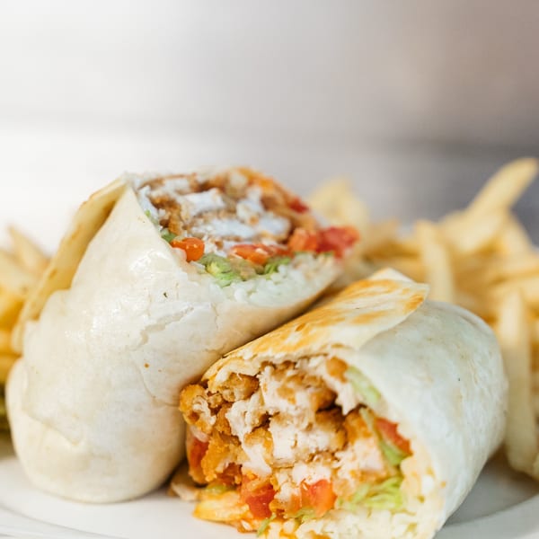 Two chicken wraps filled with fried chicken, lettuce, and tomatoes, served with fries.