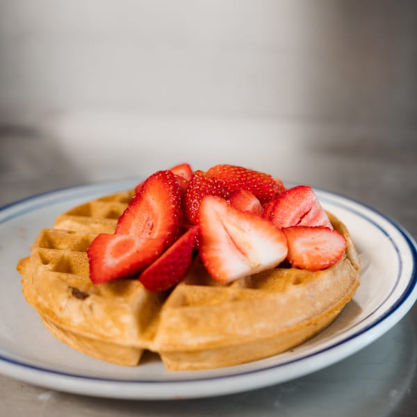 Golden waffle topped with fresh, sliced strawberries on a white plate with blue rim.