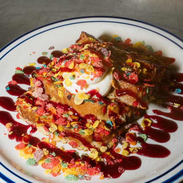 Lena's Kitchen French toast topped with colorful cereal, whipped cream, and berry syrup on a white plate.